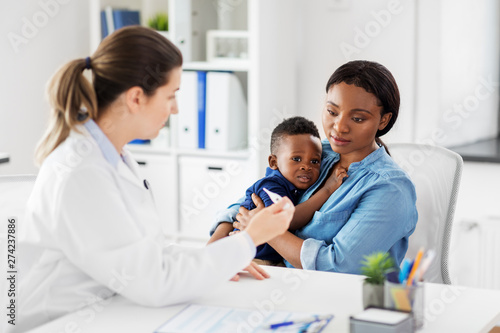 medicine, healthcare and pediatry concept - african american mother with sick baby son and caucasian doctor with thermometer at clinic