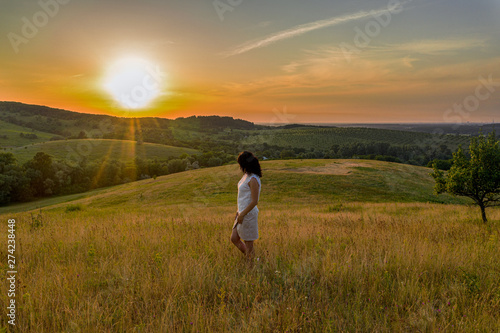 Cute brunette young woman on the summer green hills landscape