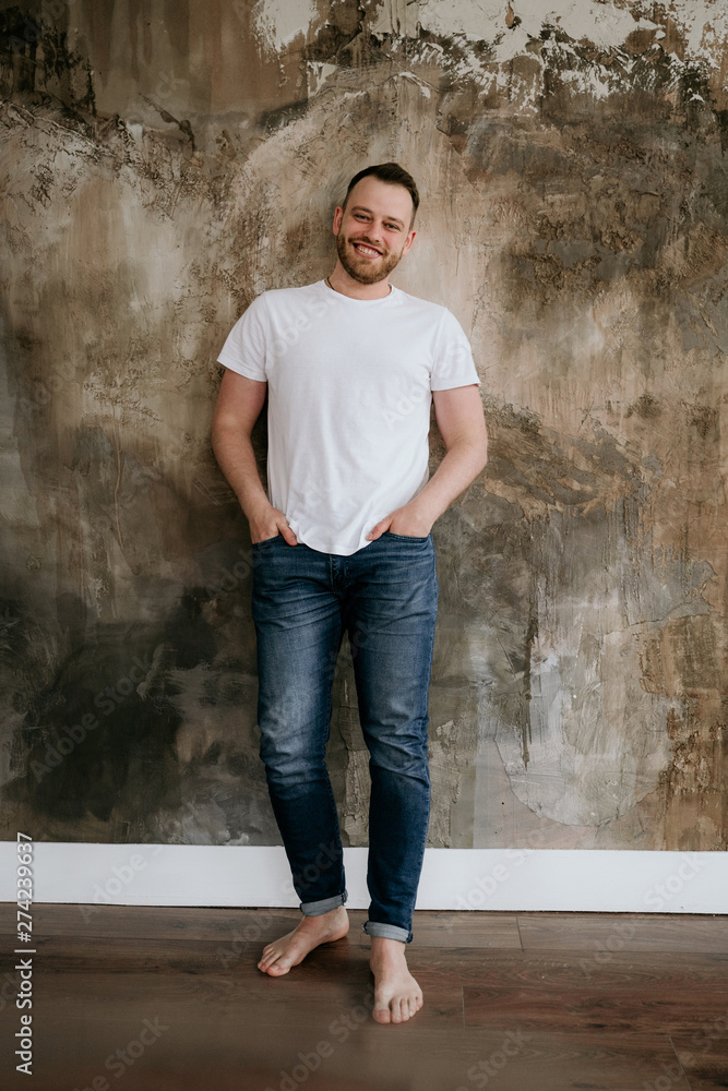 The guy smiles in jeans and a white T-shirt on a textural background. Red hair and beard. The guy smiles in jeans and a white T-shirt on a textural background. Red hair and beard.