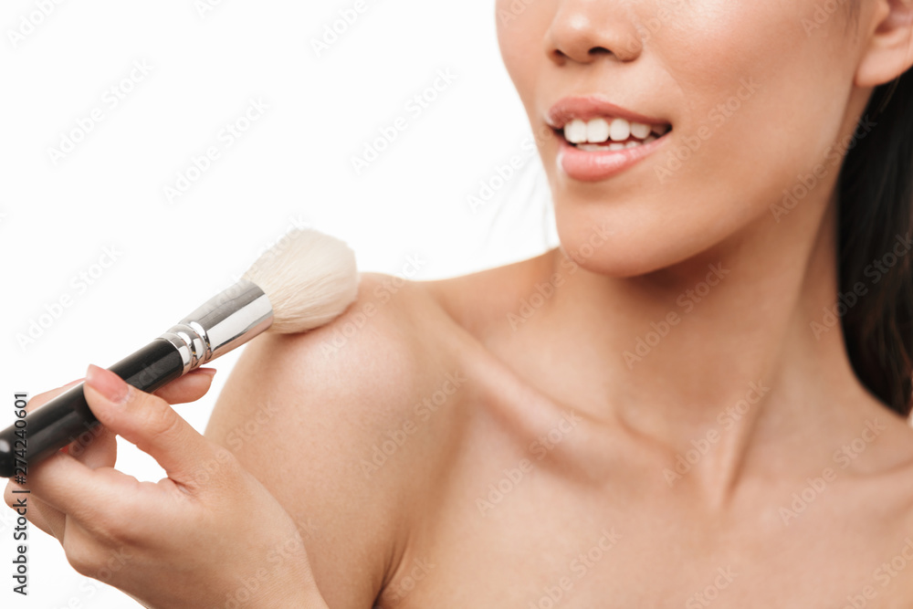 Happy young beautiful asian woman posing isolated over white wall background holding makeup brush.