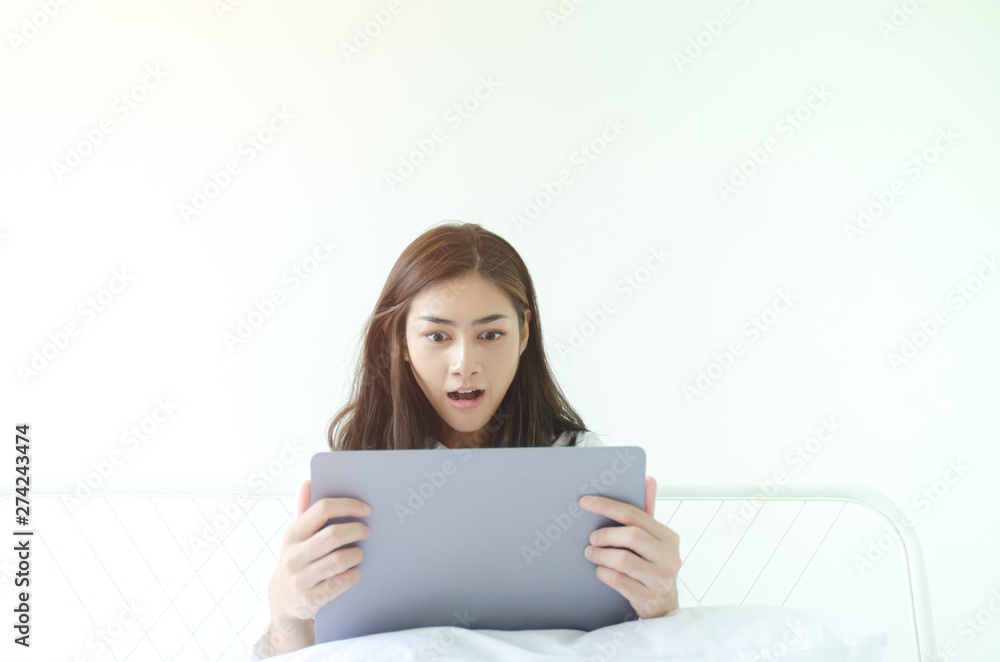 Beautiful Asian woman is smiling.Lady work with laptops on the sofa in the room in the morning.She is happy to get a new job, success, or get good news.In the white room there is a woman inside.
