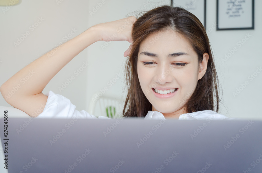 Beautiful Asian woman is smiling.Lady work with laptops on the sofa in the room in the morning.She is happy to get a new job, success, or get good news.Do not focus on the main object of this image. Beautiful Asian woman is smiling.Lady work with laptops on the sofa in the room in the morning.She is happy to get a new job, success, or get good news.Do not focus on the main object of this image.