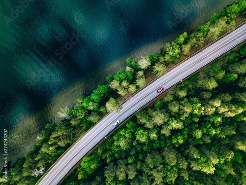 Aerial view of road between green forest and blue lake in Finland