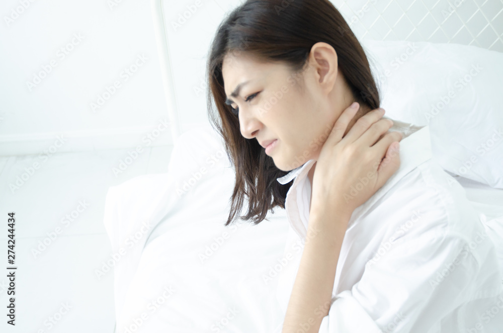 Asian women wear white pajamas in the bedroom. She has pain in the neck area. Asian women wear white pajamas in the bedroom. She has pain in the neck area.