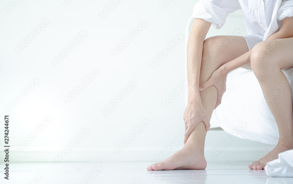 Asian girl wearing white dress have leg pain. The woman was squeezing her leg in a white bedroom with sunshine.Warm tone.Do not focus on objects. Asian girl wearing white dress have leg pain. The woman was squeezing her leg in a white bedroom with sunshine.Warm tone.Do not focus on objects.