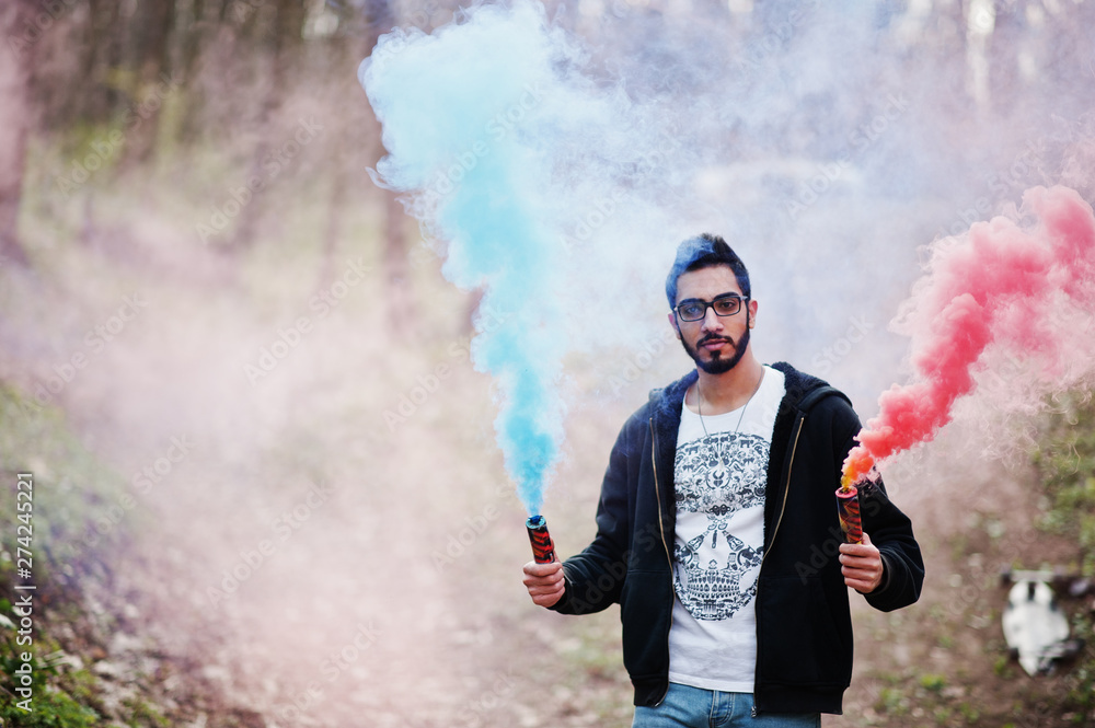Obraz premium Street style arab man in eyeglasses hold hand flare with red and blue smoke grenade bomb.