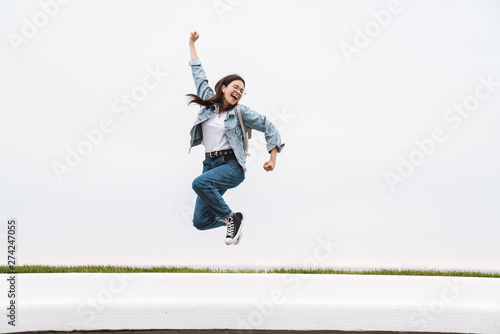 Image of cheerful teenage girl having fun and rejoicing while walking along white wall outdoors