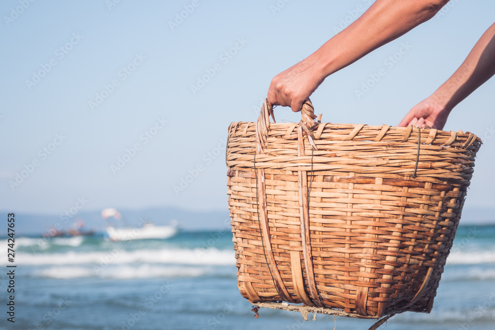 strong male hands hold a wicker basket on the background of the sea - obrazy, fototapety, plakaty 