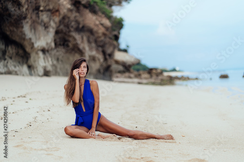 Sexy tanned model in blue swimwear posing on white sandy beach