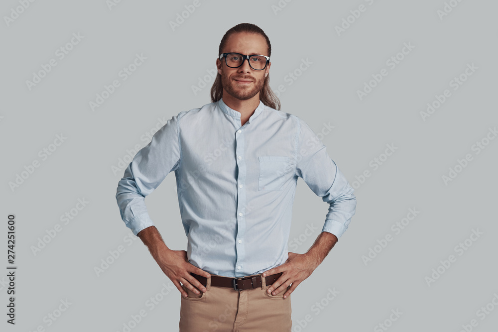 Fototapeta premium Positively charming. Handsome young man looking at camera and smiling while standing against grey background