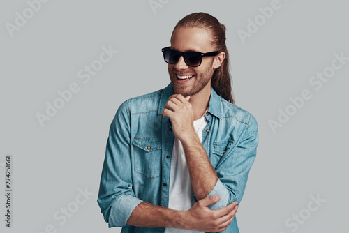 In good mood. Handsome young man looking away and smiling while standing against grey background