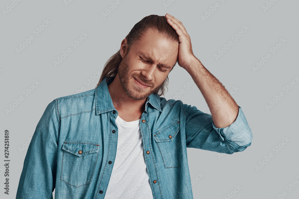 So tired. Frustrated young man keeping eyes closed and making a face while standing against grey background So tired. Frustrated young man keeping eyes closed and making a face while standing against grey background