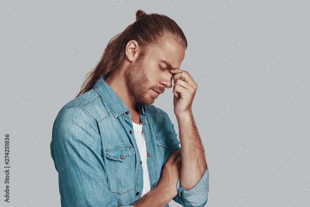 Headache. Frustrated young man keeping eyes closed while standing against grey background Headache. Frustrated young man keeping eyes closed while standing against grey background