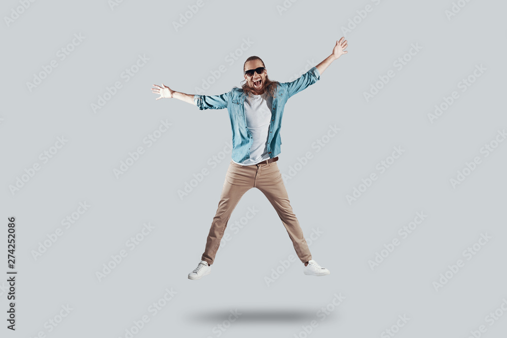 Totally free. Full length of handsome young man keeping arms outstretched while hovering against grey background Totally free. Full length of handsome young man keeping arms outstretched while hovering against grey background