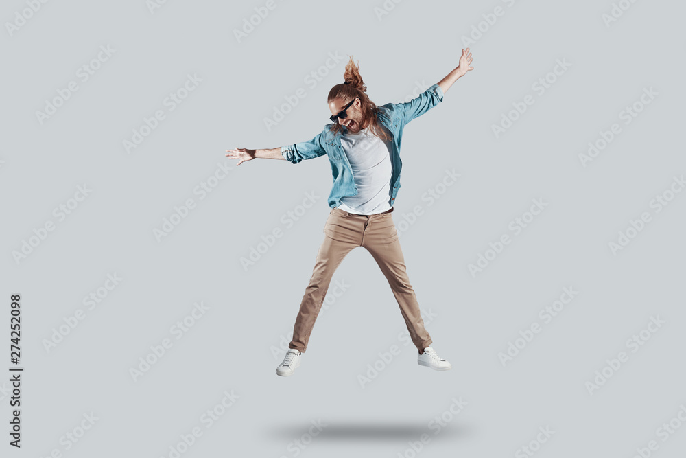 Totally carefree. Full length of handsome young man keeping arms outstretched while hovering against grey background Totally carefree. Full length of handsome young man keeping arms outstretched while hovering against grey background
