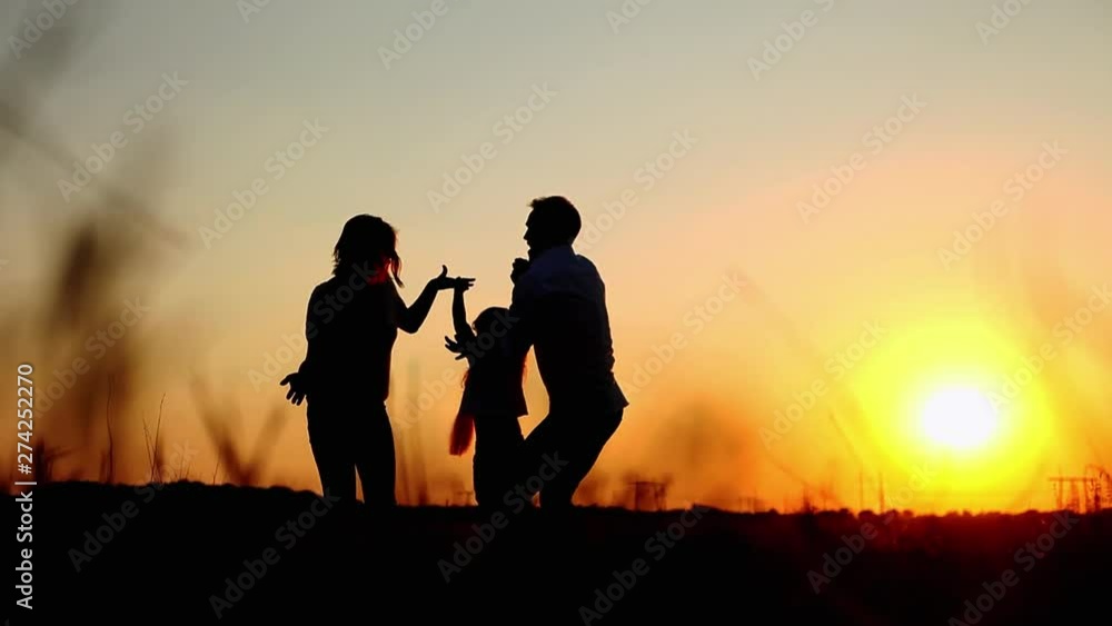 Silhouettes of happy parents throw up their daughter and hugs at summer sunset in the field, enjoying their vacation Silhouettes of happy parents throw up their daughter and hugs at summer sunset in the field, enjoying their vacation