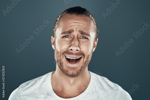 Come on! Frustrated young man looking at camera and making a face while standing against grey background