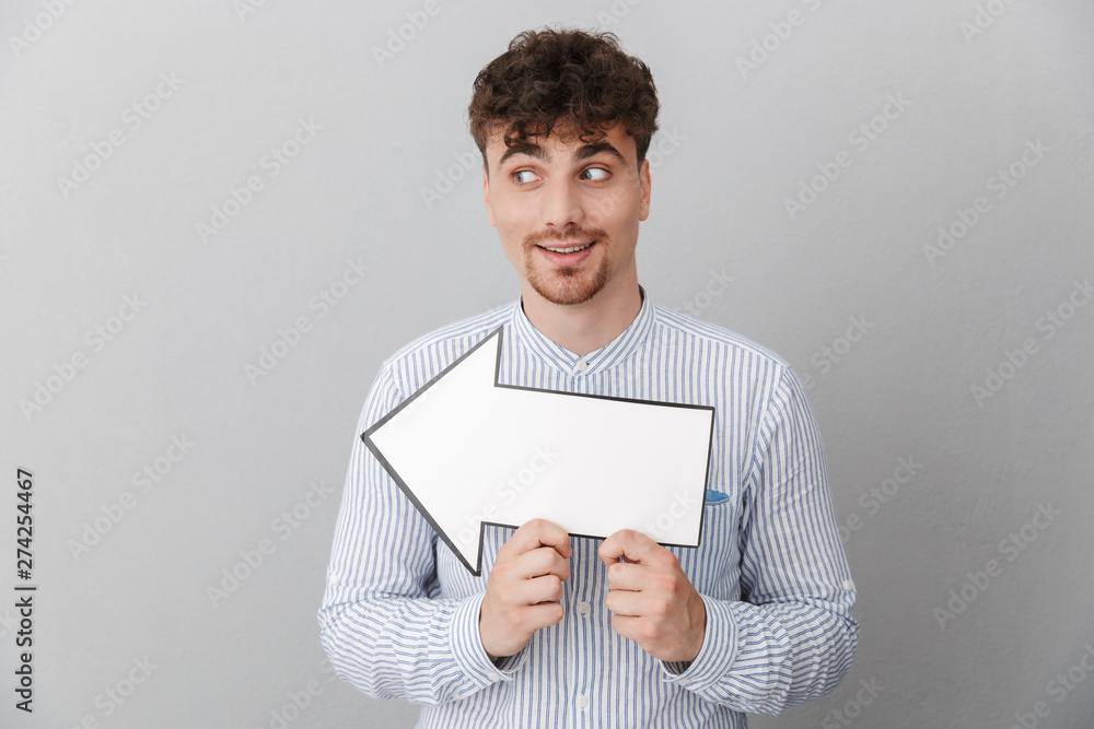 Portrait of happy beautiful man dressed in shirt holding blank copyspace arrow pointer Portrait of happy beautiful man dressed in shirt holding blank copyspace arrow pointer