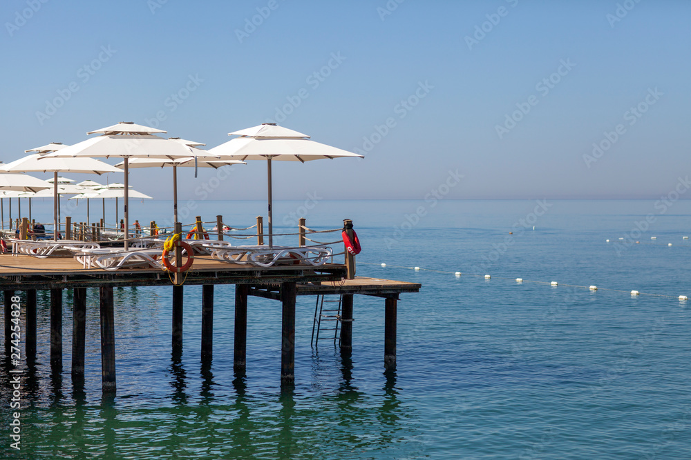 Parasols and sunbeds stand one after another on the touristic wooden pier with an infinity sea view.