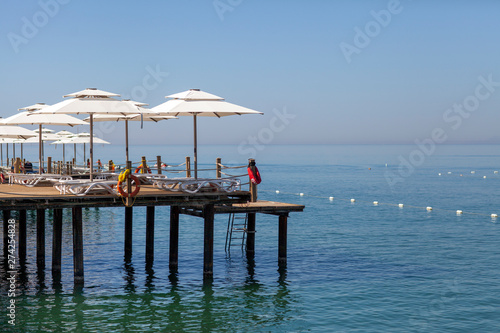 Parasols and sunbeds stand one after another on the touristic wooden pier with an infinity sea view.