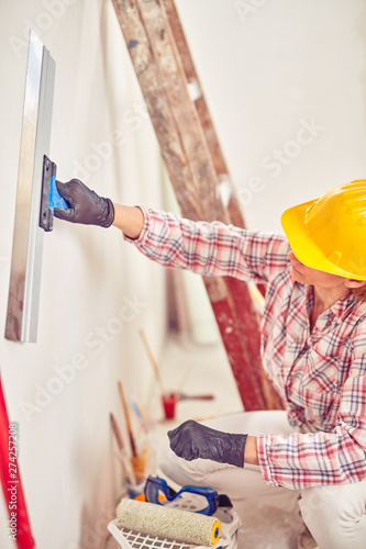 Working woman plastering / painting walls inside the house.