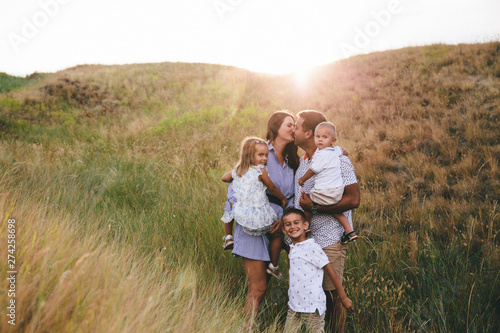 Happy dad and children hugging and having fun outdoors in a wheat field. Sunset