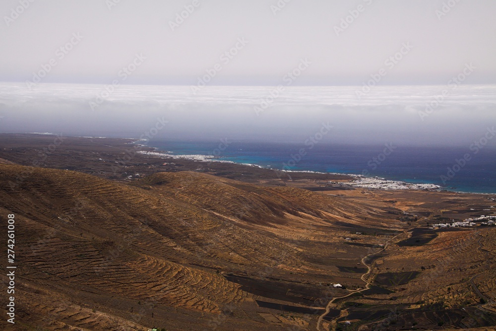View from mountain top Mirador de Haria on north east barren coast with small white village and fog over the ocean