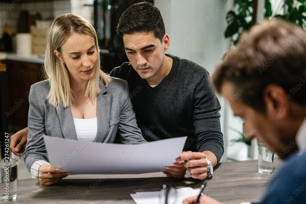 Young couple analzying blueprints while having a meeting with real estate agent. Young couple analzying blueprints while having a meeting with real estate agent.