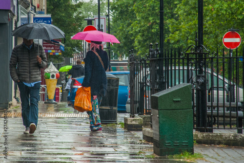Pedestrians protect themself from the rain with umbrellas during a rainfall in Chiswick street.