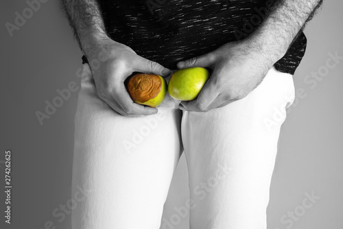 A man at the level of the genitals , holding a ripe and rotten apple. Disease for men. The concept of protection of sexually transmitted infections. Testicular cancer. Close up photo