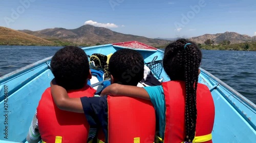 3 kids riding on a boat wearing life jackets