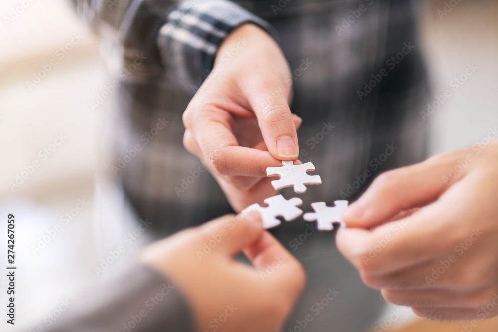 Closeup image of many people hands holding and putting a piece of white jigsaw puzzle together Closeup image of many people hands holding and putting a piece of white jigsaw puzzle together