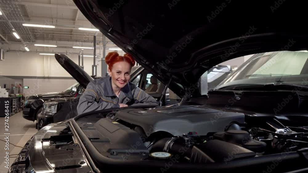 Charming female car mechanic smiling to the camera, working at the garage. Woman auto technician enjoying repairing cars at the workshop. Female equality, profession concept Charming female car mechanic smiling to the camera, working at the garage. Woman auto technician enjoying repairing cars at the workshop. Female equality, profession concept