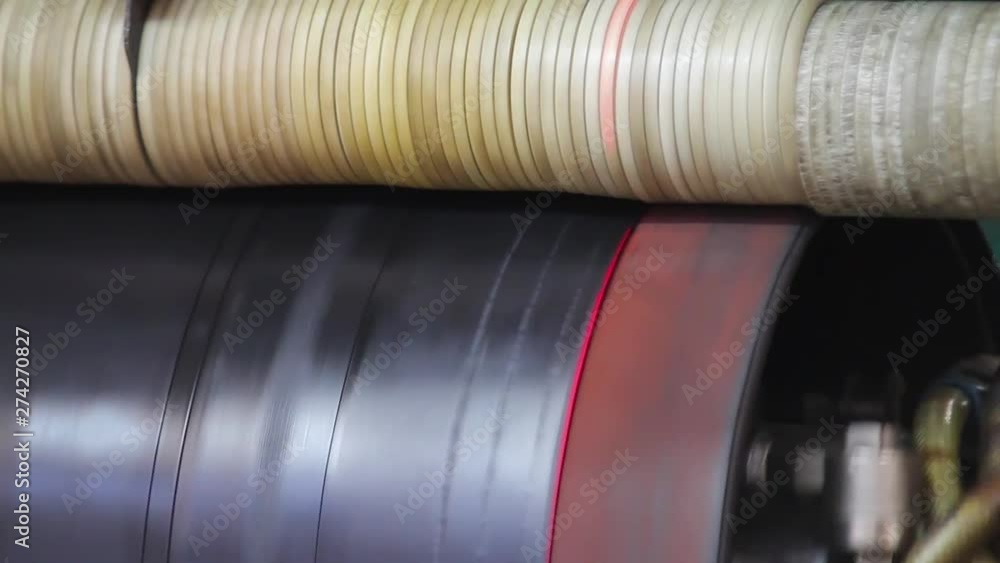 Rubber tape is reeled up on a drum in the machine. Manufacture of tires. Closeup smooth processed rubber bands pass between roller mechanism in powerful tire company. Tire production machine close up. Rubber tape is reeled up on a drum in the machine. Manufacture of tires. Closeup smooth processed rubber bands pass between roller mechanism in powerful tire company. Tire production machine close up.