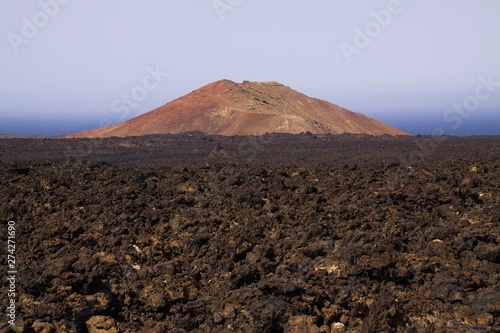 View over rough volcanic lava rocks on red cone of volcano with blurred atlantic ocean background - Timanfaya NP, Lanzarote