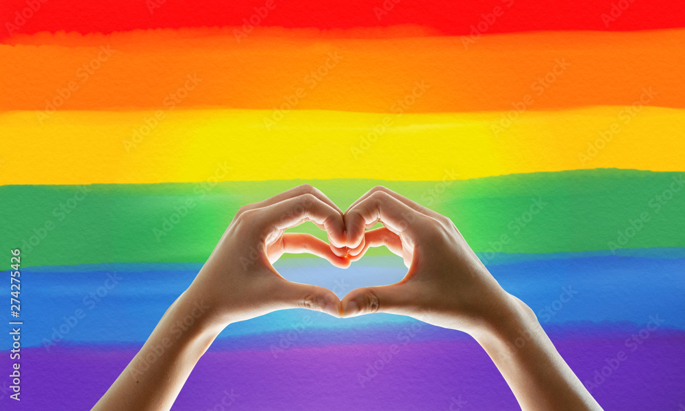 Rainbow flag, hand showing heart symbol Rainbow flag, hand showing heart symbol
