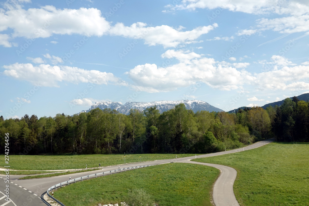 Landscape with countryside roads in foothills of the alps mountains and close up forest  under blue sky with white clouds on bright sunny day