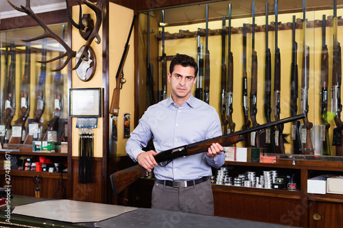 Handsome adult male owner of hunting shop offering rifle