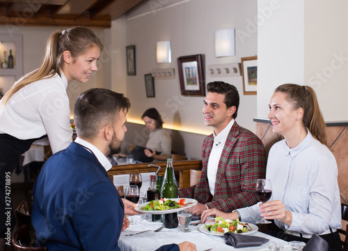 Waitress serving meals to company at restaurant