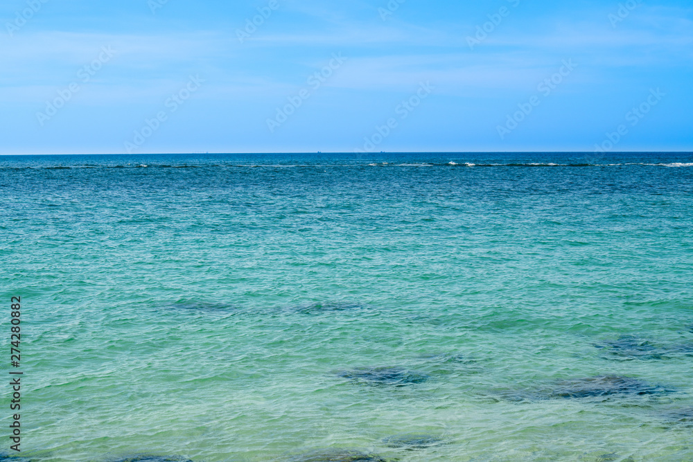 Landscape wide shot elective focus of the sun glimmering sunlight peaking the waving sea surface in hot summer sunny day with blue sky, white clouds and mountains backgrounds