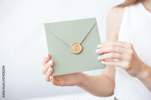 Close-up photo of female hands holding a silver blue or pink invitation envelope with a wax seal, a gift certificate, a postcard, a wedding invitation card