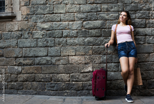 traveler with suitcase leaning against stone wall