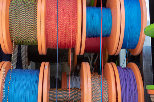 Side shot of the strings wrapped around the spool. Ropes in white, blue, red, yellow colors. Shipping and ropes used in industry