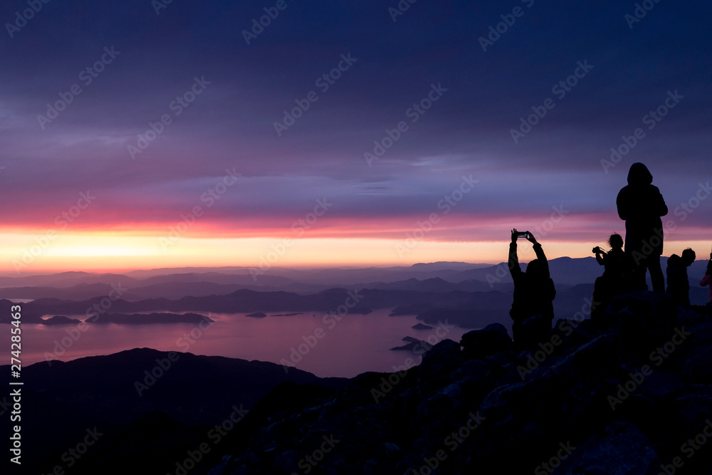 Multi-colored sunset. Silhouettes of people on top of a mountain overlooking the sea..