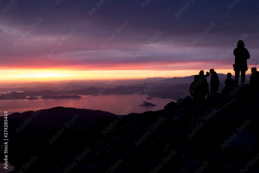 Multi-colored sunset. Silhouettes of people on top of a mountain overlooking the sea.
