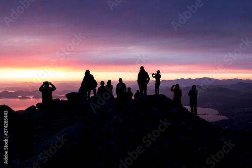 Multi-colored sunset. Silhouette of a woman with a violin. Silhouettes of people on top of a mountain overlooking the sea.