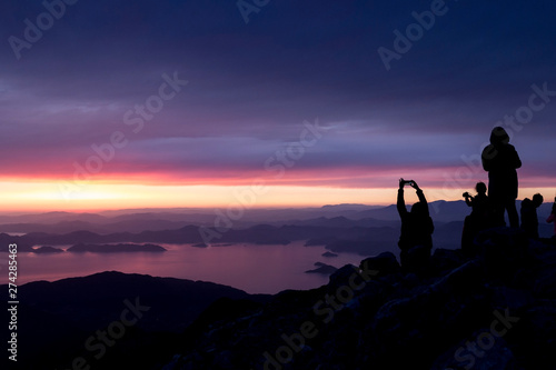 Multi-colored sunset. Silhouettes of people on top of a mountain overlooking the sea..