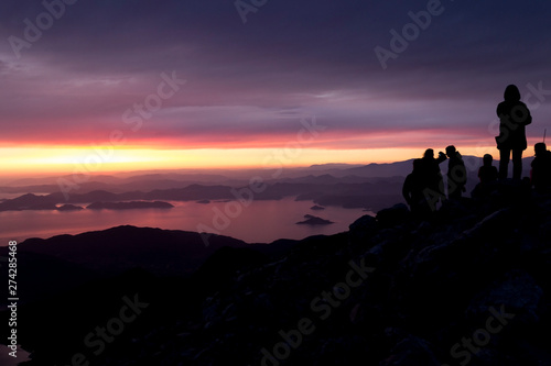Multi-colored sunset. Silhouettes of people on top of a mountain overlooking the sea.