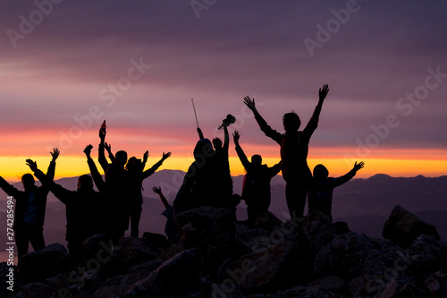 Multi-colored sunset. Silhouette of a woman with a violin. Silhouettes of people on top of a mountain overlooking the sea..