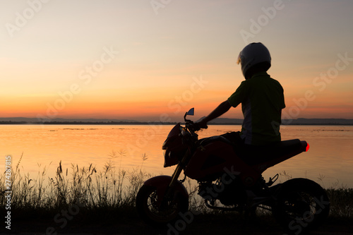 Young biker over sunset, male riding motorcycle, motorbike driver traveling, girl racing on the lake road, freedom lifestyle.Ubolrat dam,khonkaen,thailand. © krsprs